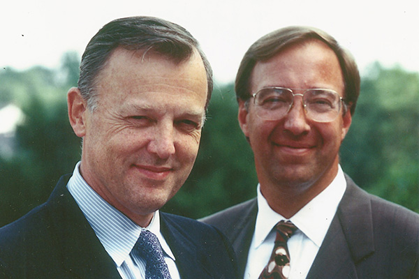 Two men in suits outdoors smiling.