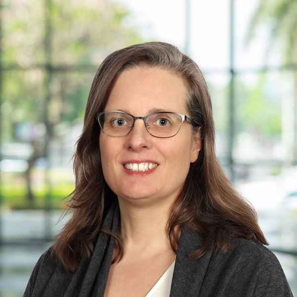 Woman smiling with glasses and long hair.