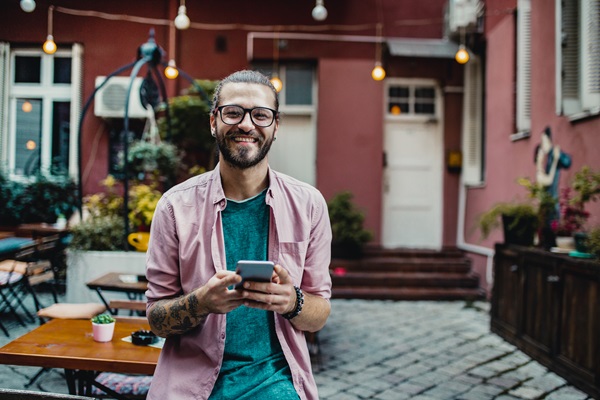 Smiling man holding phone in outdoor café.