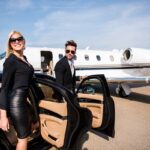 Couple exits car near private jet on runway.