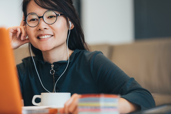 Smiling woman with earphones using a laptop.