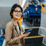 Woman holding phone and coffee on train steps.