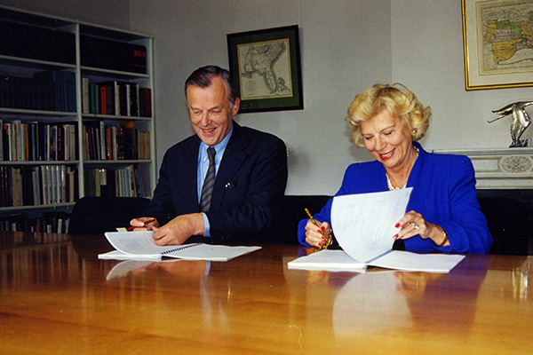 Two people signing documents at a desk.