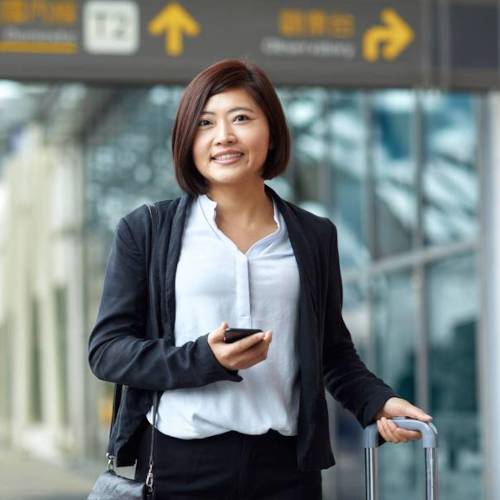 Traveler with luggage and phone at airport terminal.