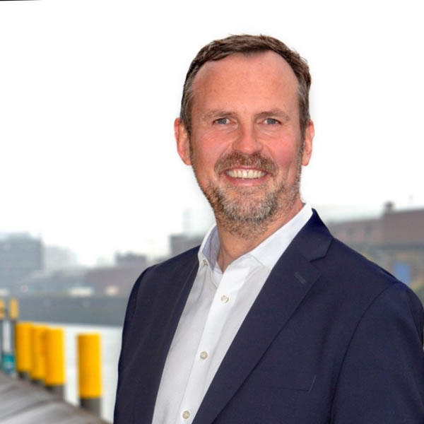 Homem sorrindo em cenário urbano nublado.